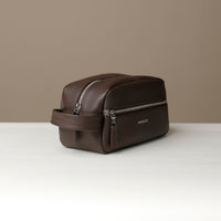 A brown toiletry bag 2014 with a silver zipper closure and a handle, with visible brand Danilos, placed against a neutral background. Lateral view. 