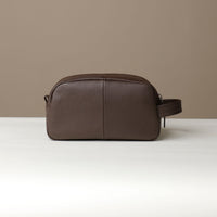 A brown toiletry bag 2014 with a silver zipper closure and a handle, placed against a neutral background. Back view.