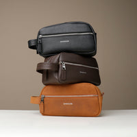 Stack of three toiletry bags 2014 in black, brown, and tan colors, made of premium leather with multiple zippered compartments, with visible brand Danilos. 
