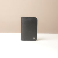Front view of a black passport case lovable in pebble leather with a Danilos logo on a beige background