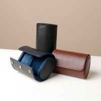 Three oval-shaped watch cases, one black and one brown, made of leather with a fabric lining, designed to hold watches.