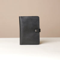 Front view of a black Danilos pebble leather inskspirator with a clip closure on a beige background