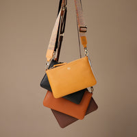 Stack of leather handbags with patterned strap on a brown background