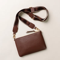 Brown leather crossbody bag with a strap on a light beige background