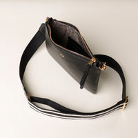 Black leather crossbody bag with a strap on a light gray background