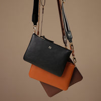 Black, brown, and orange handbags stacked on a beige background