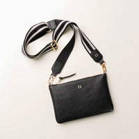 Black leather bag with a striped strap on a light beige background