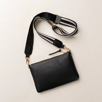 Black leather crossbody bag with a striped strap on a light beige background