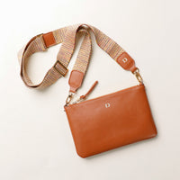 Brown leather clutch with a woven strap on a light background