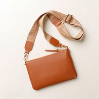 Brown leather handbag with a woven strap on a light beige background