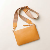 Yellow handbag with a patterned strap on a light beige background