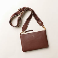 Brown leather bag with a matching strap on a light beige background