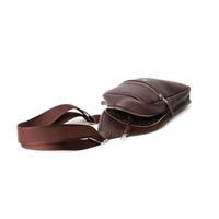 upper view of an open chocolate brown sling pack andres with silver zipper and the Danilos logo over a white background