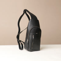Side view of an open Danilos leather sling pack Andres in a black color with silver zippers on a beige background