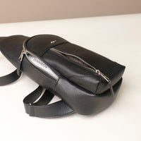 Close-up view of an open Danilos leather sling pack Andres in a black color with silver zippers on a beige background