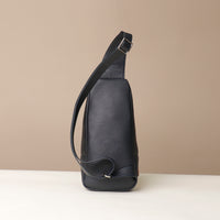 Back view of a Danilos leather sling pack Andres on a marine blue and brown color with silver zippers on a beige background