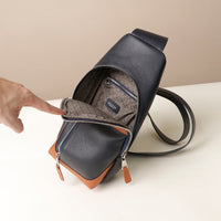 Close-up view of an open Danilos leather sling pack Andres on a marine blue and brown color with silver zippers on a beige background