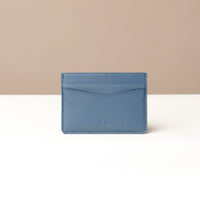 A blue card holder with a minimalist design, featuring multiple card slots and a center slot for cash or extra cards, made from premium leather.