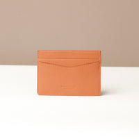 Tan leather cardholder on a white surface with a beige background