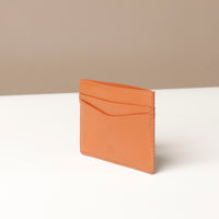 Tan leather cardholder on a white surface with a beige background