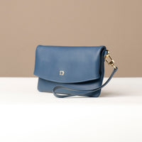 Side view of a blue leather Karelia Clutch Danilos with a visible hand strap over a white and beige background