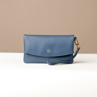 Front view of a blue leather Karelia Clutch Danilos with a visible hand strap over a white and beige background