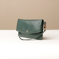 Side view of a green leather Karelia Clutch Danilos with a visible hand strap over a white and beige background
