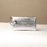 Back view of a silver leather Karelia Clutch Danilos with a visible zipper over a white and beige background