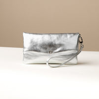 Front view of a silver leather Karelia Clutch Danilos with a visible hand strap over a white and beige background