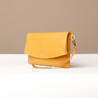 Side view of a yellow leather Karelia Clutch Danilos with a visible hand strap over a white and beige background
