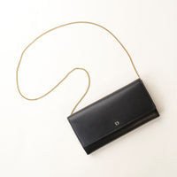 front view of a danilos clucth versaviva in black leather with a gold chain strap in a beige background