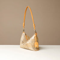 Gold crossbody Danilos bag with a strap on a beige background