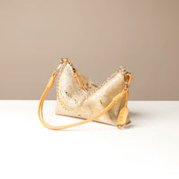 Gold crossbody Danilos bag with beige strap on a white surface against a beige background