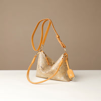Gold and yellow crossbody Danilos bag with a strap on a white surface and beige background