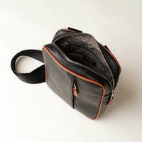 upper view of a open zipper danilos black and brown crossbody dylan bag over a beige background
