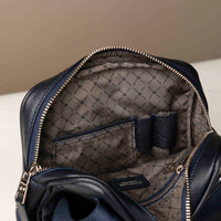 close up view of a open danilos navy blue crossbody dylan bag with organizing pockes inside over a beige background
