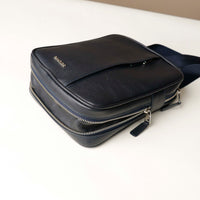 close up view of a open expandable zipper pocket of a danilos navy blue crossbody dylan bag over a beige background