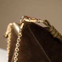 Close-up of a green suede Danilos handbag with a gold chain and clasp on a neutral background