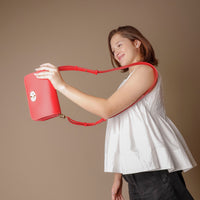girl grabbing a red crossbody bag smiling with white shirt