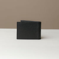 Back view of a Danilos pebble black leather money clip Steven, in a beige and white background