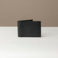 Front view of a Danilos pebble black leather money clip Steven, in a beige and white background