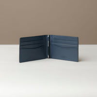 Front view of an open Danilos pebble marine blue leather money clip Steven, with 6 card slots, in a beige background