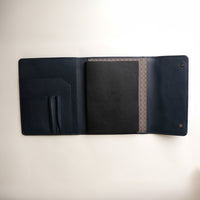 Danilos Carry-Master Portfolio in Marine leather with foldable design with a textured strap on a beige background