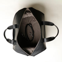 Upper view of an open black danilos hegarty travel bag with silver accents and a visible strap over a beige background