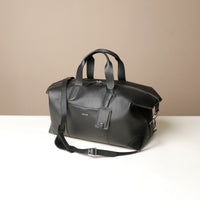front view of Two black and brown danilos hegarty travel bag with a visible strap over a beige background