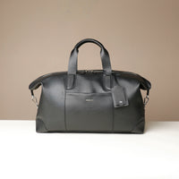 front view of a black danilos hegarty travel bag with silver accents over a beige background
