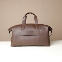 Back view of a brown danilos hegarty travel bag with a visible strap to attach to a suitcase over a beige background