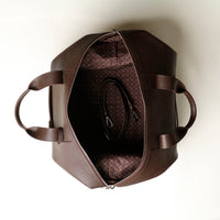 upper view of an open brown danilos hegarty travel bag with silver accents and a visible strap over a beige background