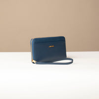 side view of a blue Danilos wallet Carlota with a visible handle drop and a gold zipper in a beige background